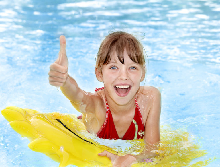 Pool Scouts - Girl sitting on inflatable ring in swimming pool giving a thumbs up